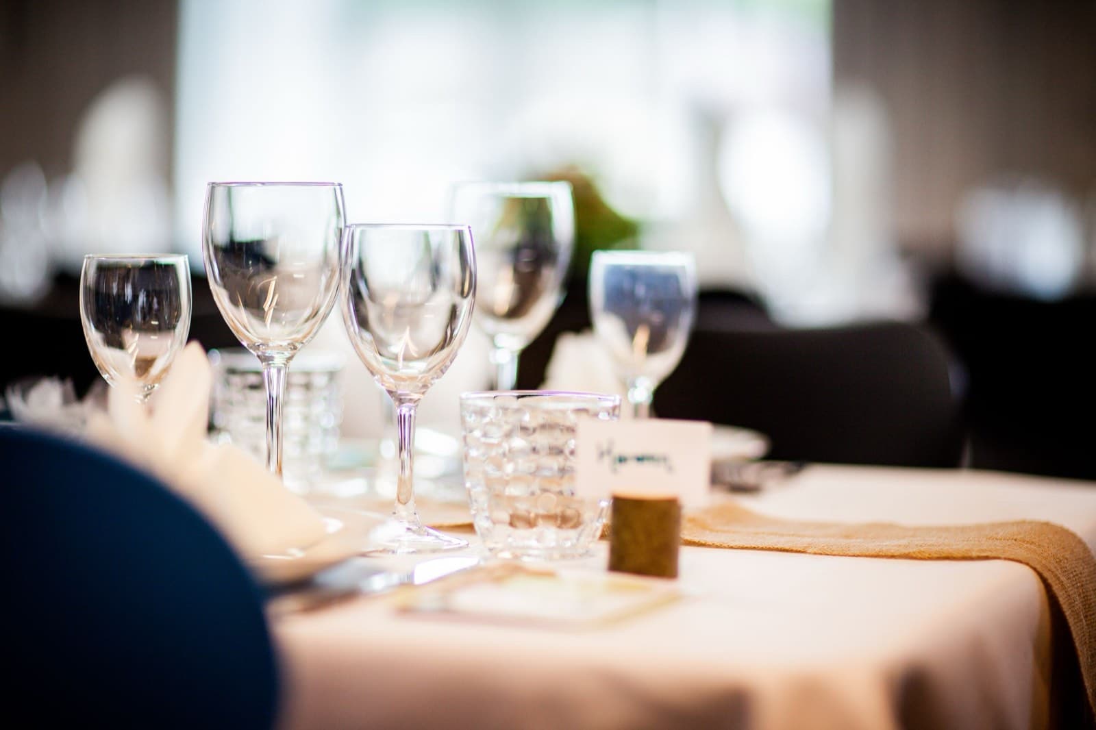 Rows of polished glassware and a handwritten place card on a linen-draped table in soft window light